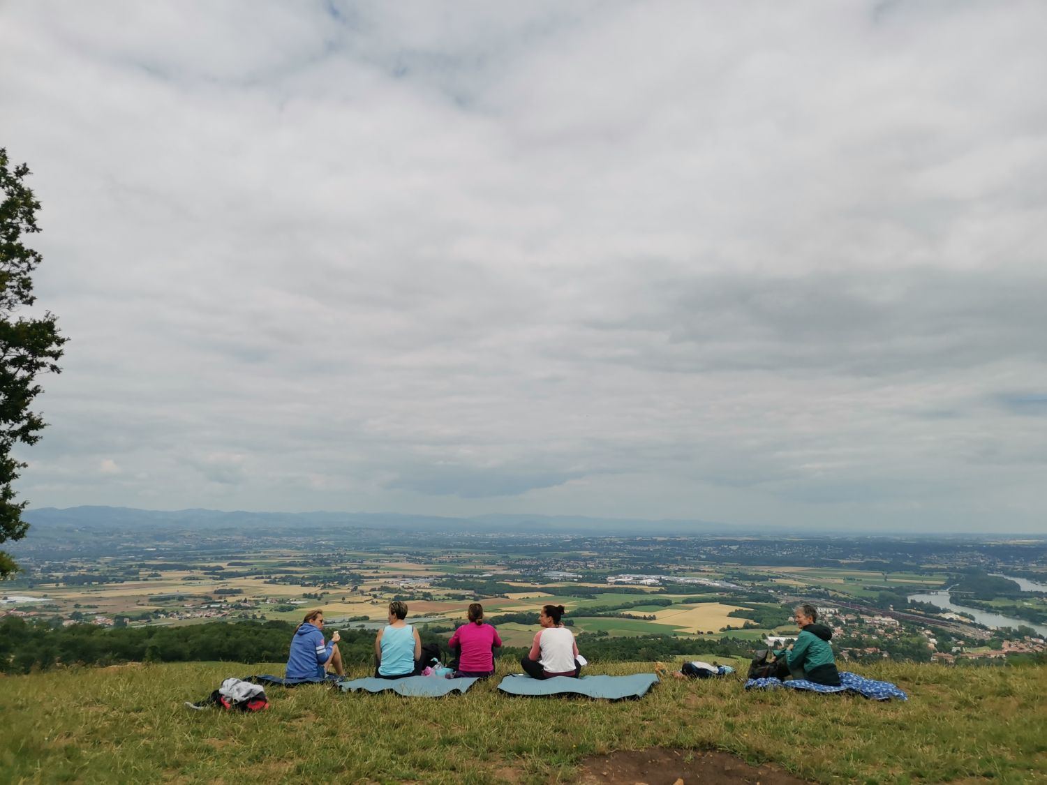 Un groupe assis dans l'herbe face à la plaine, au terme d'une marche